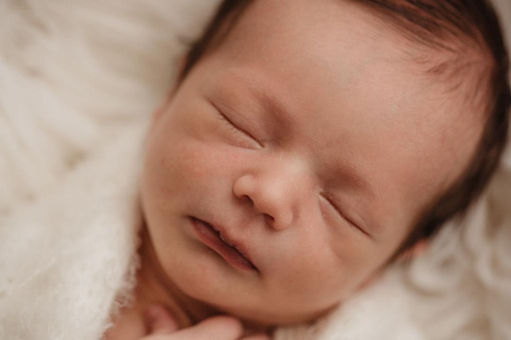 Bebê recém-nascido acomodado em cestinha durante ensaio newborn