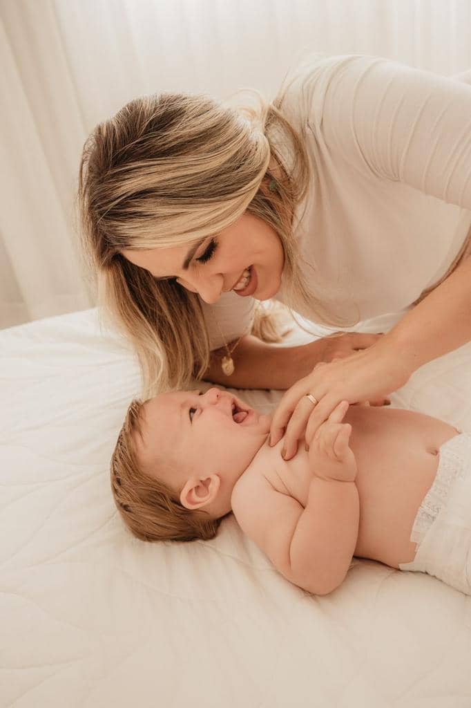 Mãe brincando com o bebê sorridente em ensaio de acompanhamento