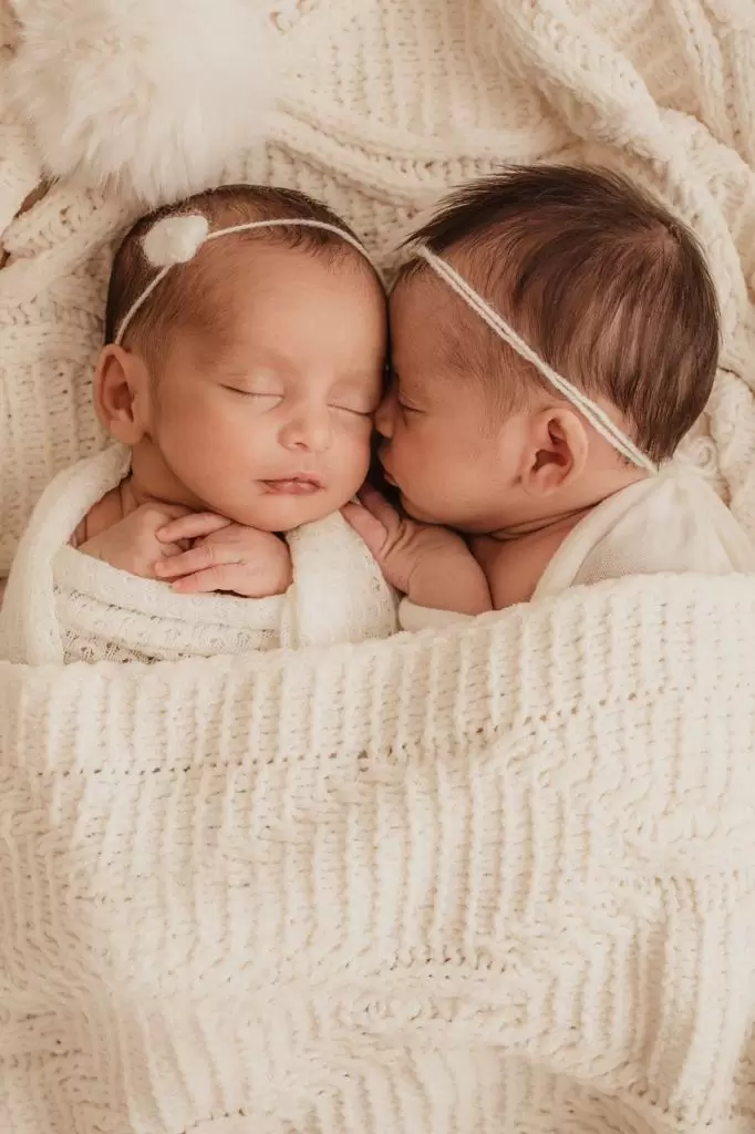 Gêmeas recém-nascidas dormindo juntas em ensaio newborn