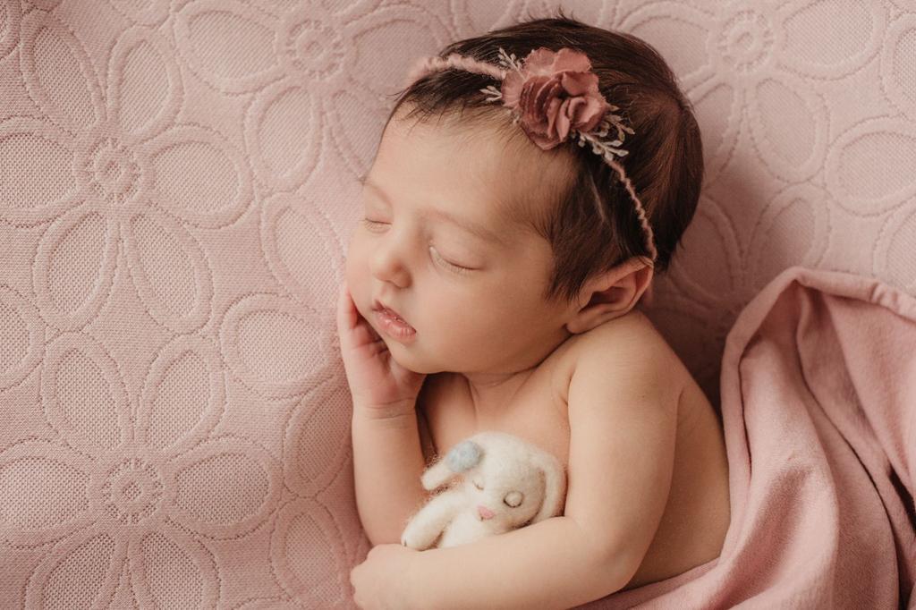 Recém-nascida com faixa de flor em cenário rosa durante ensaio newborn